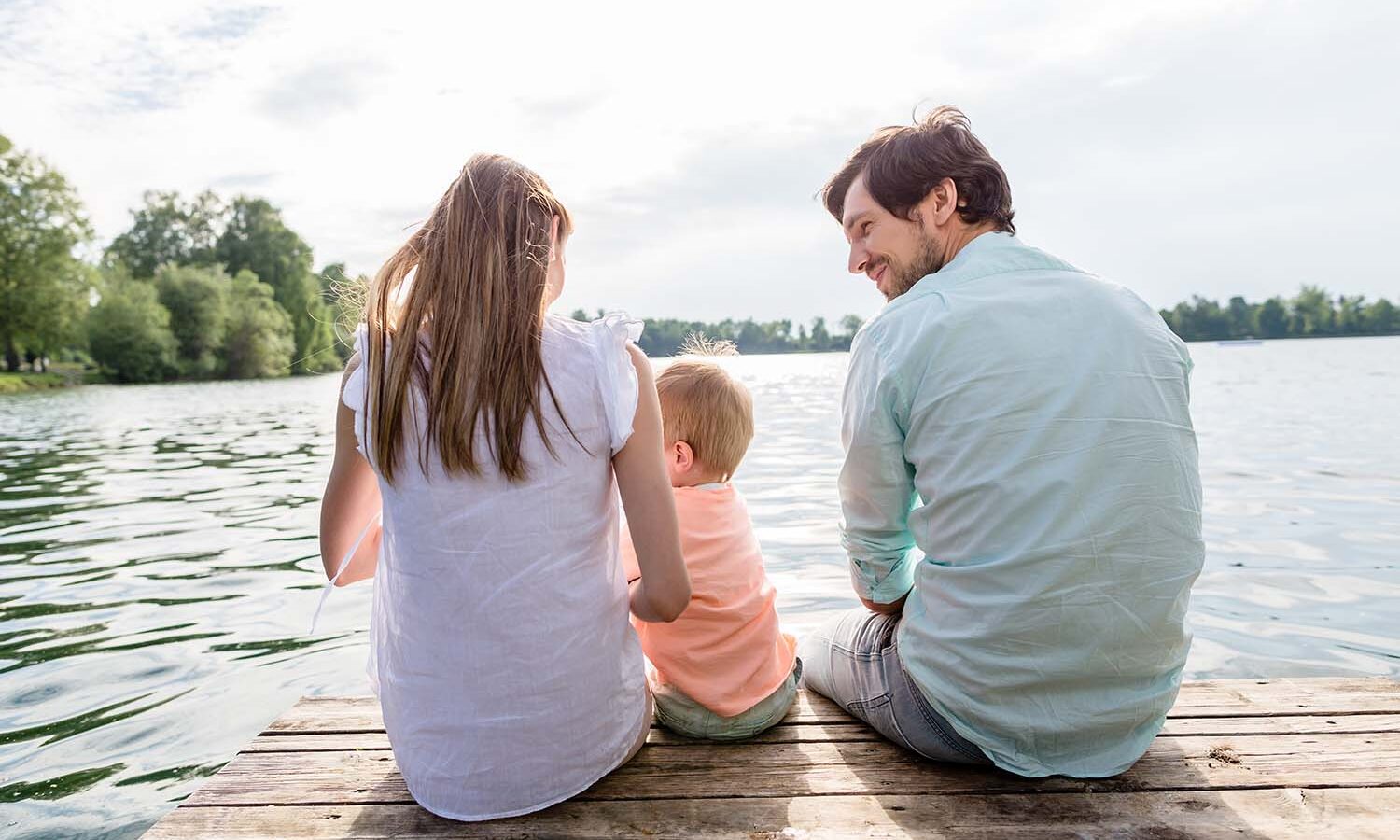 Family sitting on jetty of pond or lake in summer